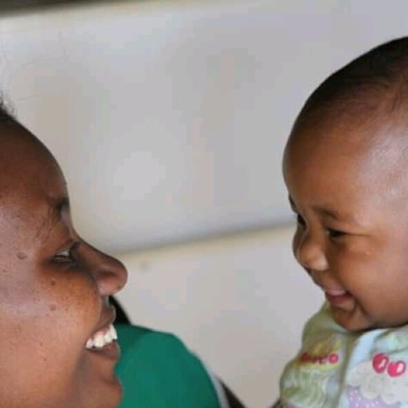 A close-up photograph of a mother and young child smiling warmly at each other. Their faces are turned toward one another, capturing a joyful and intimate moment of connection, love, and shared happiness.